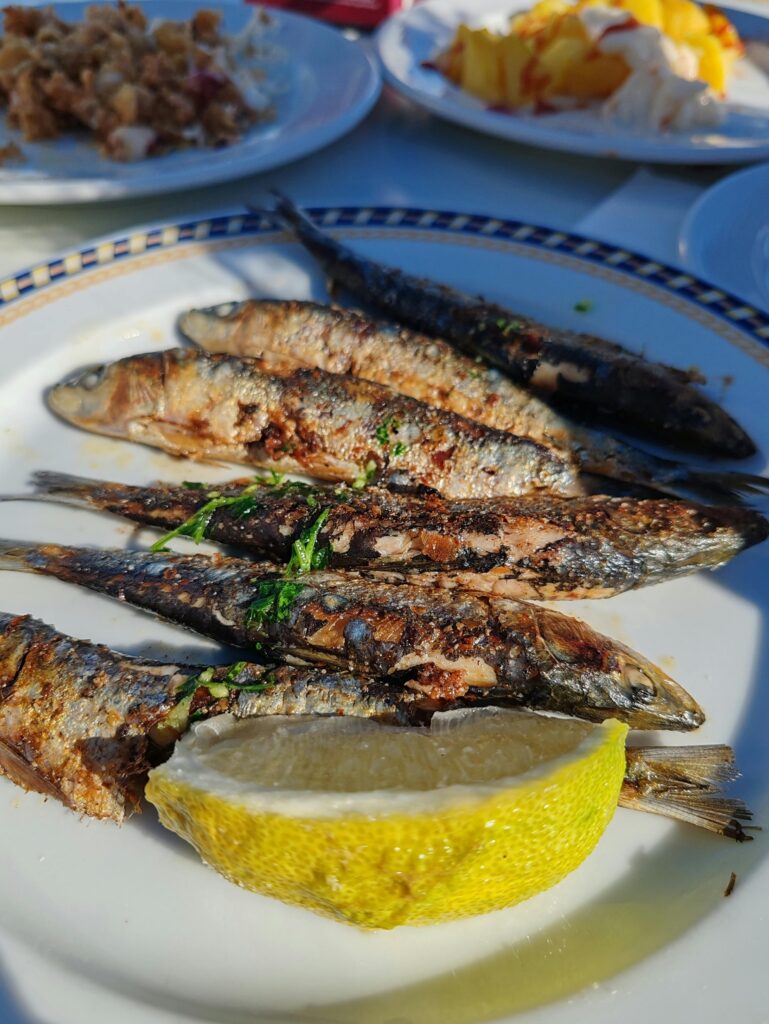 Delicious grilled sardines garnished with herbs and lemon wedge on a white plate.