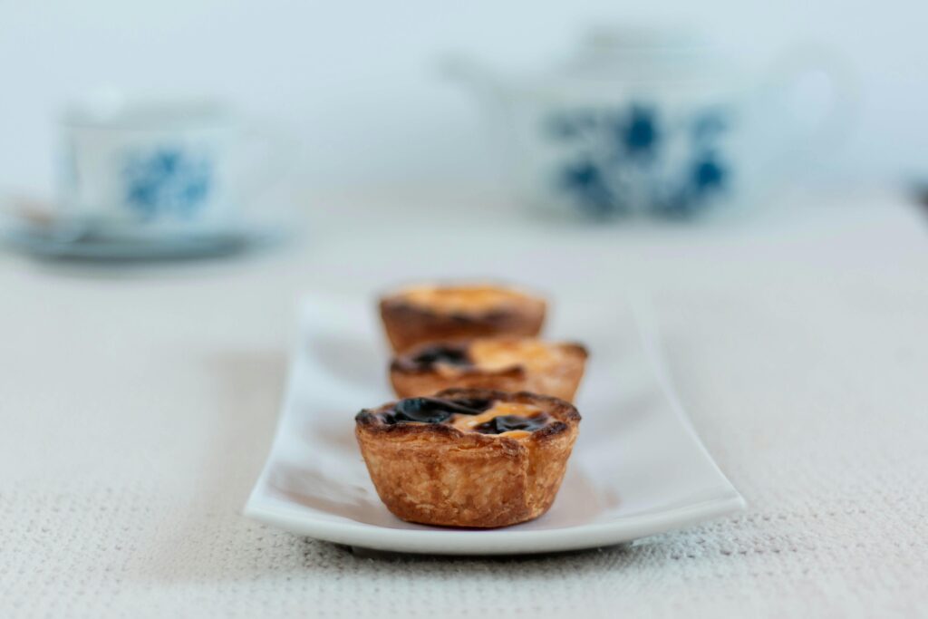Three Portuguese egg tarts on a ceramic tray with a teapot background.