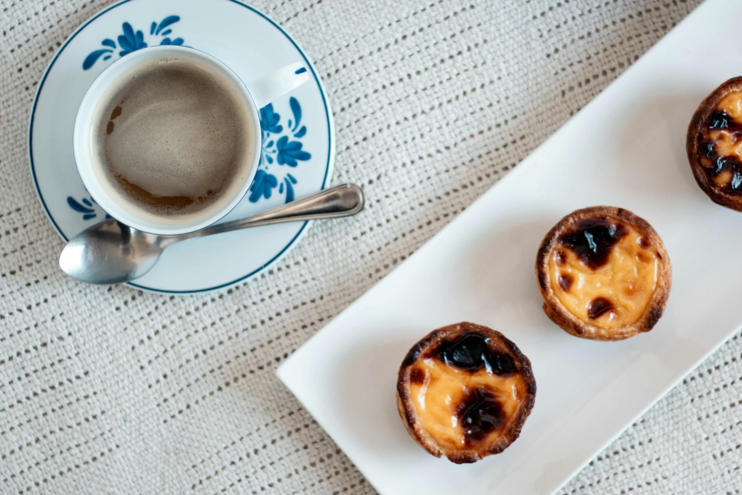 Top view of pastel de nata and coffee on a patterned cloth, perfect for gourmet food imagery.